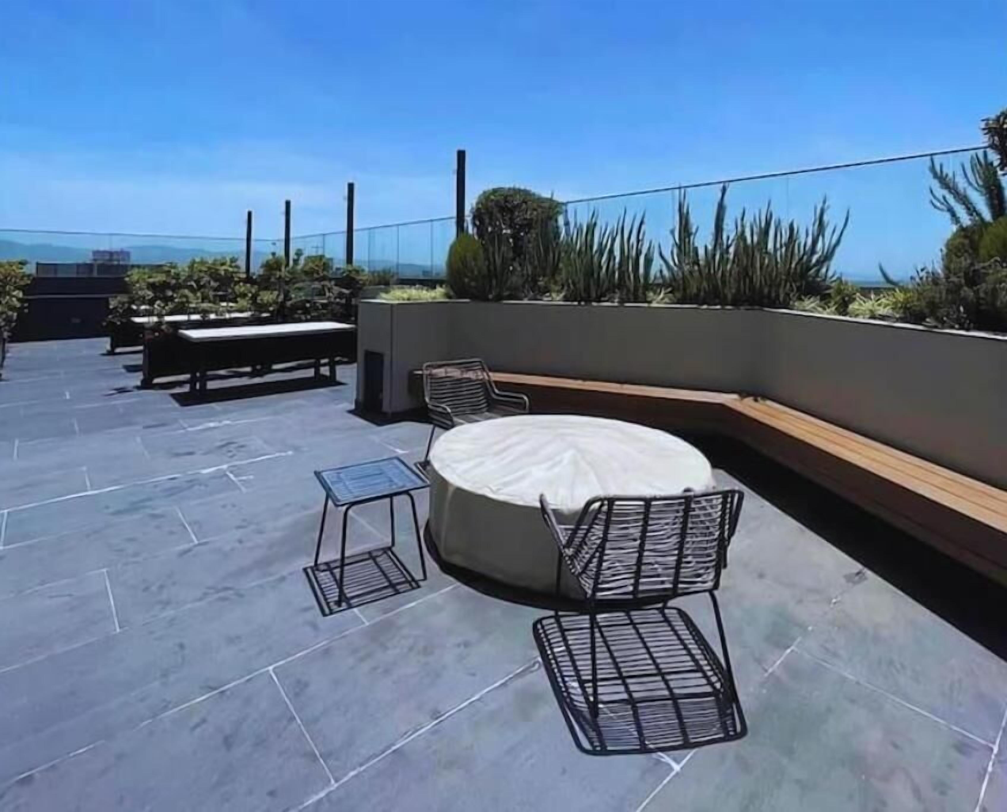 Un espacio al aire libre con una mesa redonda y sillas, un banco y una mesita.