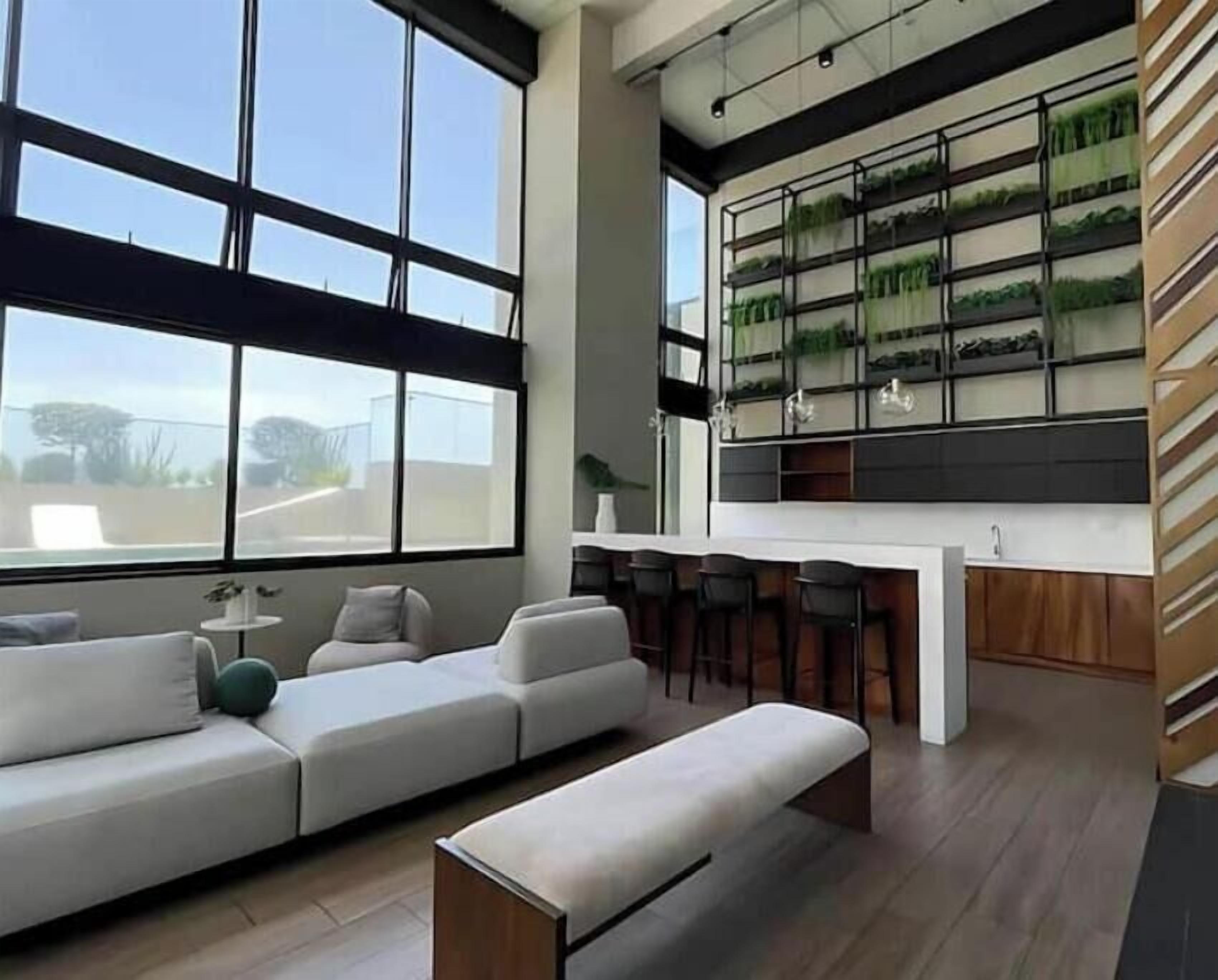 A modern living area with a large window, a sofa, a coffee table, and a kitchen area with a bar.