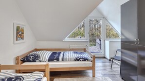 Een slaapkamer met een hoogslaper, een radiator, een raam met uitzicht op bomen, en een deur naar een balkon.