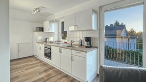 Een moderne keuken met witte kastjes, een houten aanrechtblad en uitzicht op een balkon met een hekwerk.