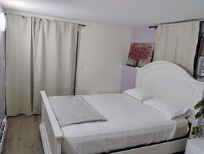 Une chambre avec un lit simple, une tête de lit blanche, une table de chevet et un tableau accroché au mur.