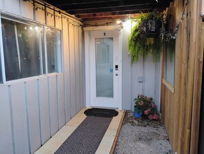 A narrow entrance with a door marked '3', a small step leading to a door mat, and a potted plant with pink flowers. - Cozy 2 Bedrooms, Mountain View Private suite (Vernon)