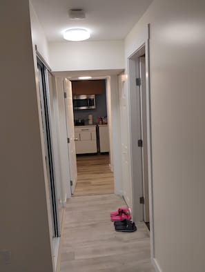 A narrow hallway leading to a kitchen with wooden flooring and a microwave.