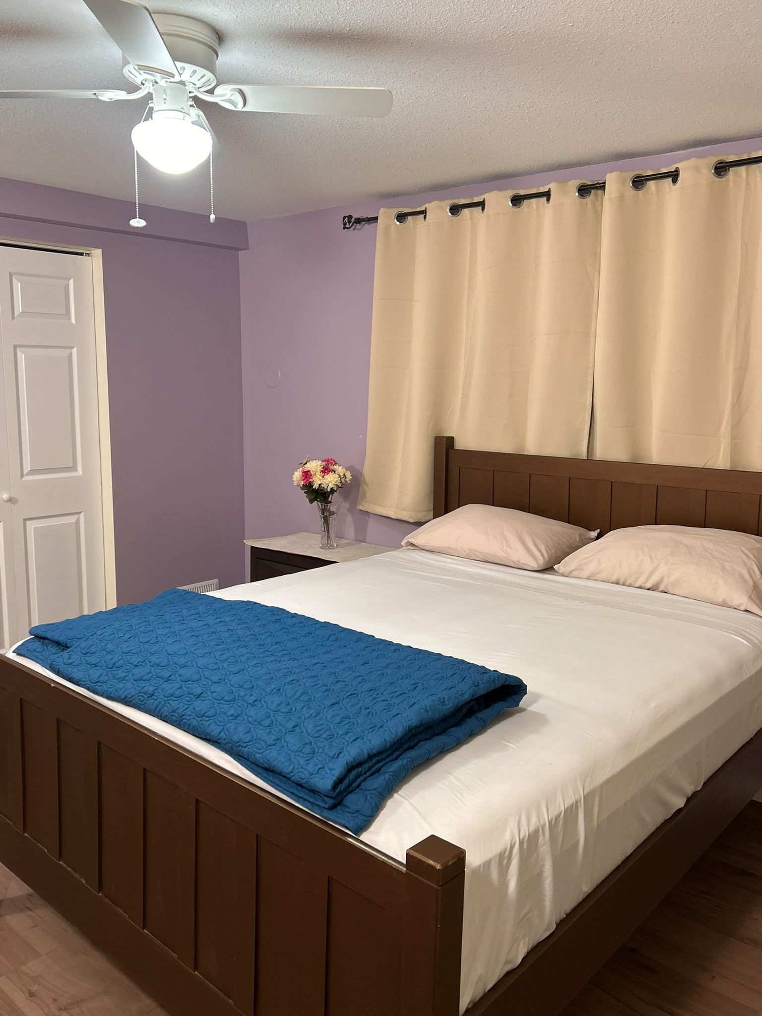 A bedroom with a bed, a nightstand, a vase with flowers, and a ceiling fan.