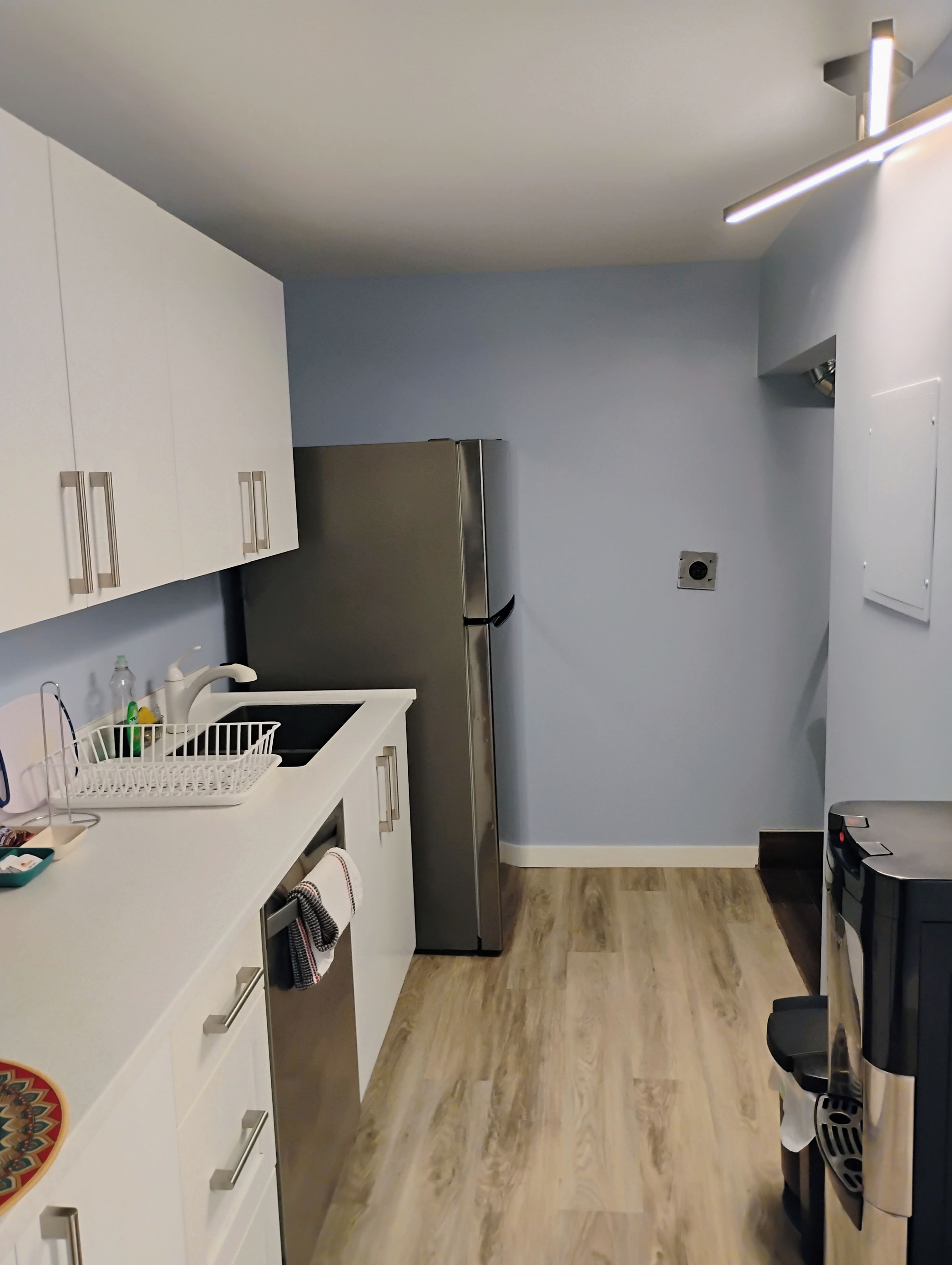 Une cuisine de taille réduite avec des meubles blancs, un réfrigérateur en acier inoxydable, un évier et un plancher en bois.