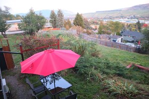 A red umbrella over a table with chairs, surrounded by a grassy area and trees.