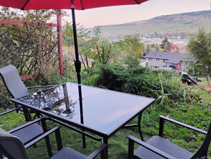 Une table avec un plateau en verre, des chaises, un parasol rouge et une vue sur un paysage rural.