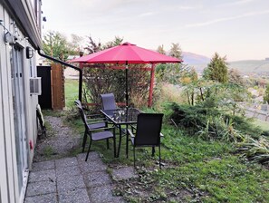 Une terrasse extérieure avec une table et des chaises, un parasol rouge et une vue sur le paysage environnant.
