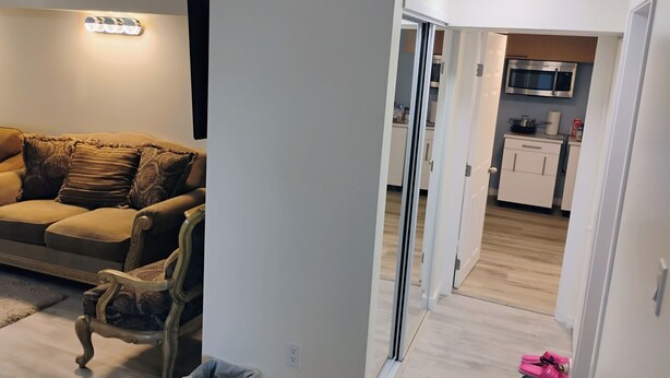 Un salon comprenant un canapé, un fauteuil, une poubelle et un coin cuisine avec des placards et des appareils électroménagers.