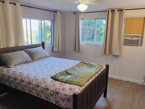 A bedroom with a bed, two windows, a ceiling fan, and an air conditioning unit.