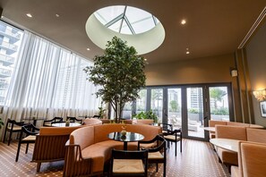 Eine moderne Lounge mit runden Tischen, Sofas und einem großen Baum.
