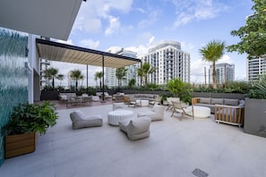 A rooftop patio with outdoor seating, palm trees, and a view of high-rise buildings. - The Crosby #308 Elegant Urban Studio (Miami)