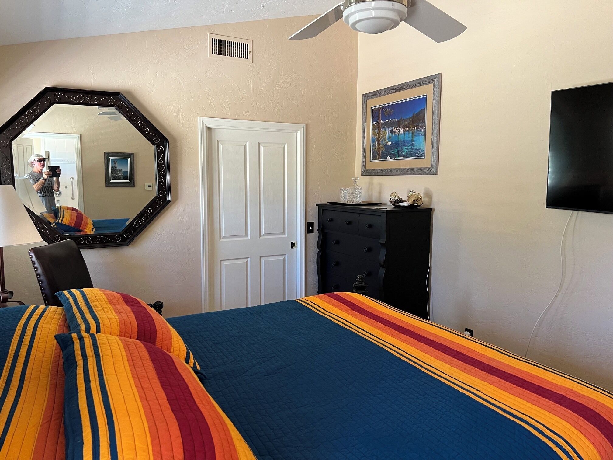 A bedroom with a bed, a dresser, a mirror, a door, and a ceiling fan.
