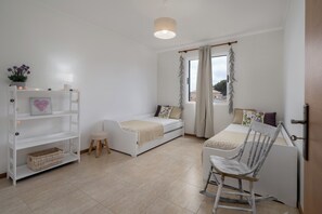 Une pièce comprenant un lit, une chaise, une petite table, une étagère et une fenêtre avec des rideaux.