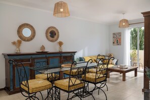 Un coin repas avec une table en verre et des chaises en métal, un buffet bleu et deux miroirs fixés au mur.