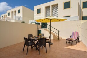 Un patio con una mesa, sillas, un paraguas amarillo y una silla a rayas.