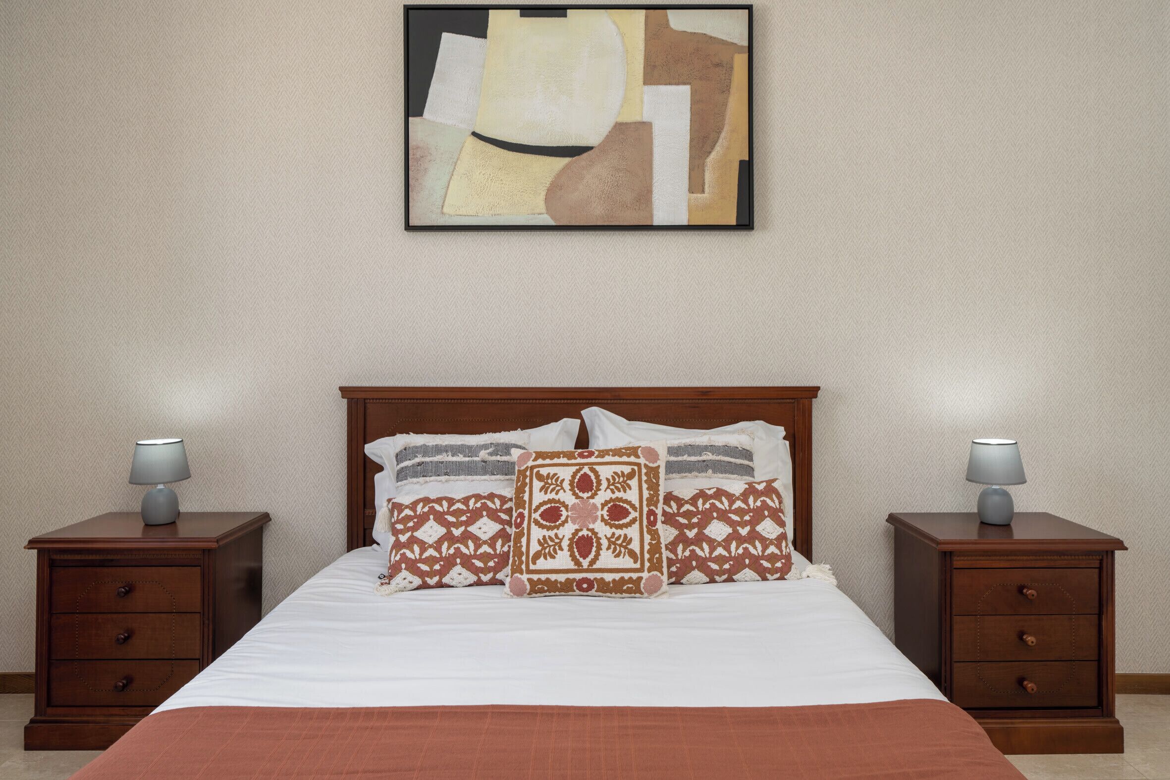 A hotel room with a large bed, two nightstands, and a framed abstract painting on the wall.