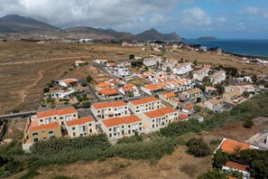 Un quartier résidentiel situé sur la côte, avec des maisons aux toits recouverts de tuiles rouges, entouré de collines et bordé par la mer.