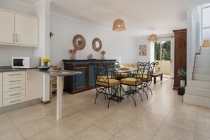 Una cocina con armarios blancos, una isla azul y una zona de comedor con cuatro sillas y una mesa.