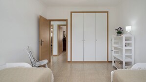 Een kamer met een bed, een stoel, een kledingkast en een wit wandrek met een lamp.