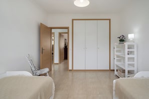 A room with a bed, a chair, a wardrobe, and a white shelving unit with a lamp.