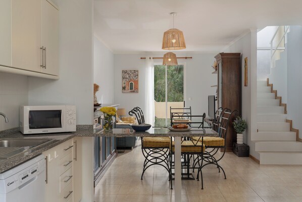 A modern kitchen with a microwave, dining table, chairs, and a hanging light fixture.