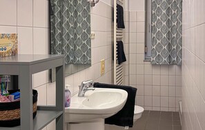 Ein Badezimmer mit einem weißen Waschbecken, einem Spiegel, einem Handtuchhalter und blickdichten Vorhängen.