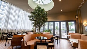 A modern lounge area with round tables, cushioned seating, a large central plant, and a skylight. - The Crosby #2012 - Luxury 1 Master Bedroom (Miami)