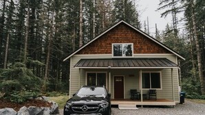 Une cabane avec un toit en pente, une véranda à l’avant et un véhicule garé devant.