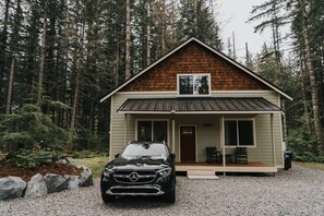 Une cabane avec un toit en pente, une véranda à l’avant et un véhicule garé devant.