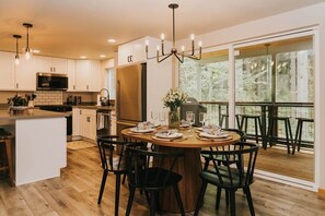 A modern kitchen with a central island, dining table with chairs, and a view of a deck with outdoor seating. - Luxury Chalet • Infrared Sauna + Hot Tub • 10 min to Park (Ashford)