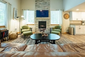 Una sala de estar con chimenea, dos sillones verdes, una mesa de centro negra y un sofá.