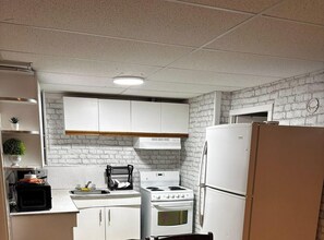 Una cucina con mobili bianchi, un fornello, un frigorifero e un muro in mattoni.