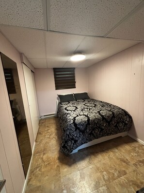 Una camera da letto con un letto, una finestra con persiane, una porta e un pavimento piastrellato.
