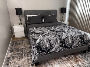 Camera da letto con un letto, due comodini, un tavolino e una coperta a motivi, oltre a una finestra con tende.