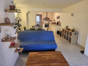 Ein Wohnzimmer mit blauem Sofa, Holzböden, einer Küche im Hintergrund und einem Essbereich.
