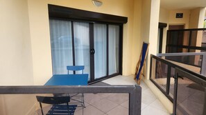 Ein Balkon mit Tisch und Stuhl, eine Schiebetür aus Glas und ein hölzernes Staffelei.