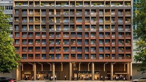 Ein mehrstöckiges Hotel mit modernem Design, das Balkone mit Pflanzen, einen Eingangsbereich im Erdgeschoss und eine Glasfassade aufweist.