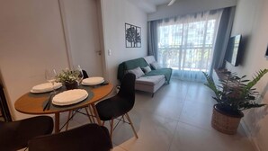 Ein Essbereich mit einem Tisch für zwei Personen, einer Couch, einem Blumentopf und einem Fenster mit Vorhängen.