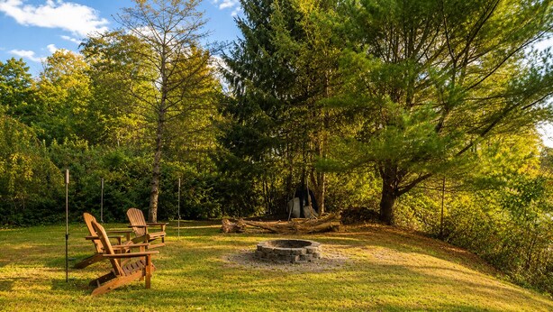 Ein Campingplatz mit Feuerstelle, zwei Adirondack-Stühlen und einem Picknicktisch.