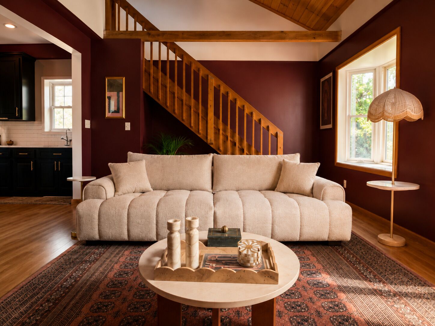 Un salon avec un escalier en bois, un canapé beige, une table basse ronde agrémentée d’objets décoratifs et un tapis à motifs.