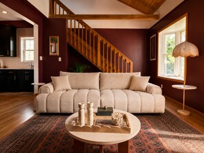 A living room with a wooden staircase, a beige sofa, a round coffee table with decorative items, and a patterned rug. - Catskill Creek w/ Deck & Views (Jefferson Heights)