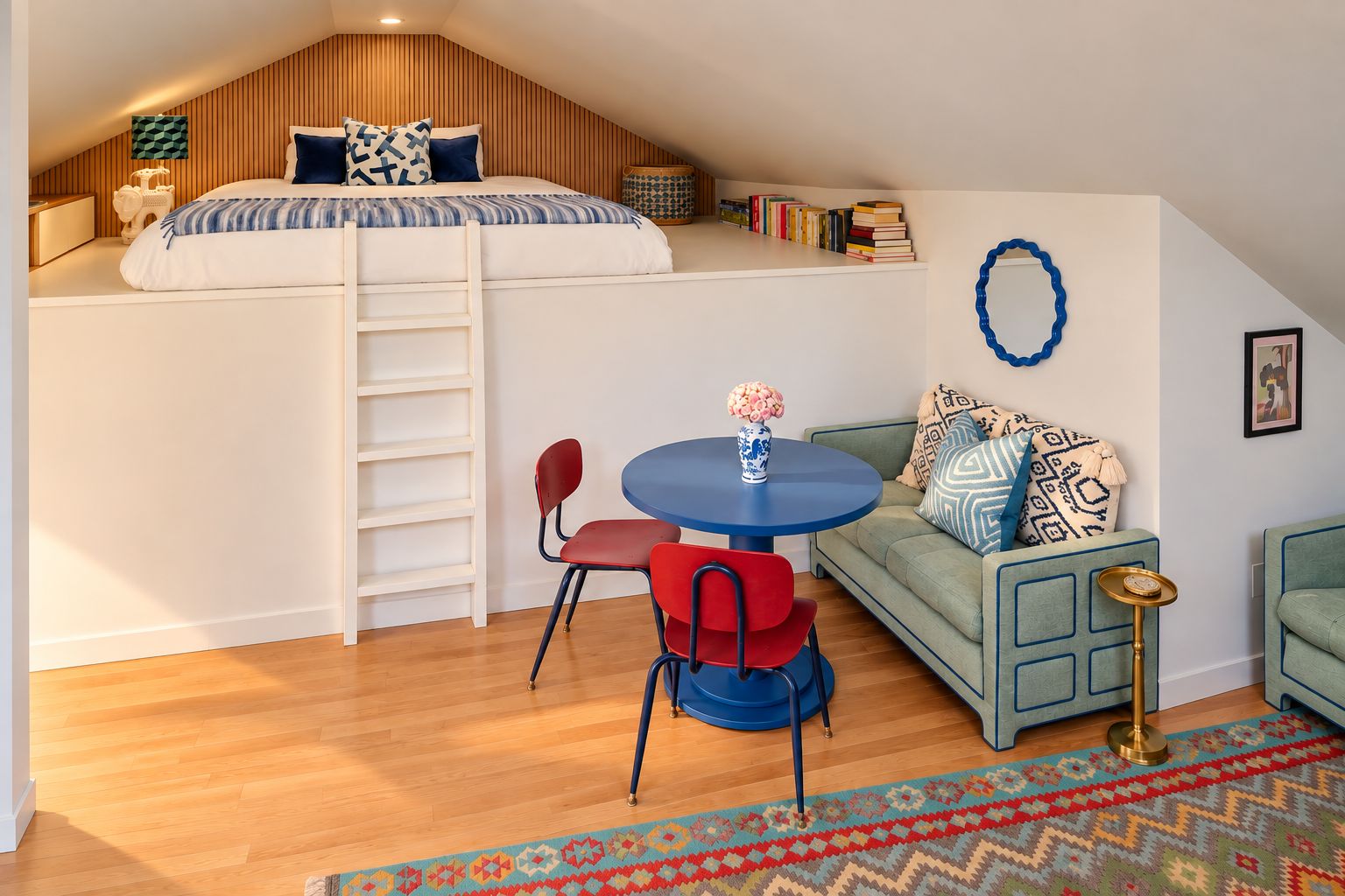 A loft bedroom with a bunk bed, a small dining table, a sofa, and a decorative wall.