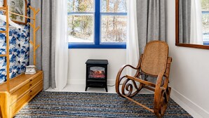 A room with a blue-framed window, a wooden rocking chair, a small black heater, and a wooden dresser with a patterned rug. - Catskills Getaway Nature Views Fire Pit (Jefferson Heights)