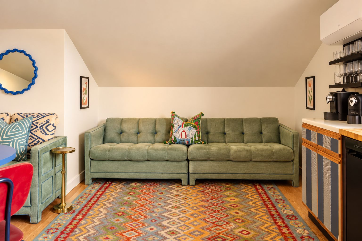 A cozy living room with a green sofa, a patterned rug, and a coffee machine on a counter.