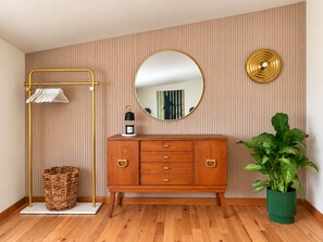 A room with a wooden floor, a wooden cabinet with drawers, a round mirror, a floor lamp, a green potted plant, and a wicker basket. - Creekview Catskill Lodge & Mountain Views (Jefferson Heights)