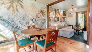 Zona de dinar amb taula rodona, cadires i un mural de vegetació tropical.