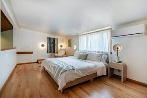 A bedroom with a bed, bedside tables, a chair, a painting, and an air conditioning unit. - Creekview Catskill Lodge w/ Canoes & Mtn Views (Jefferson Heights)