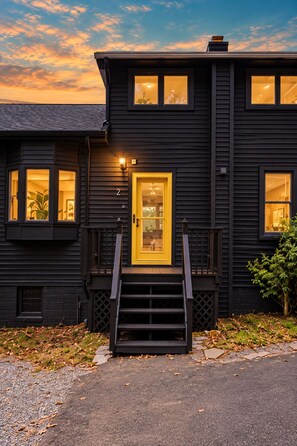 A two-story building with a dark exterior, a yellow door, and a staircase leading to the entrance. - Creekview Catskill Lodge & Mountain Views (Jefferson Heights)
