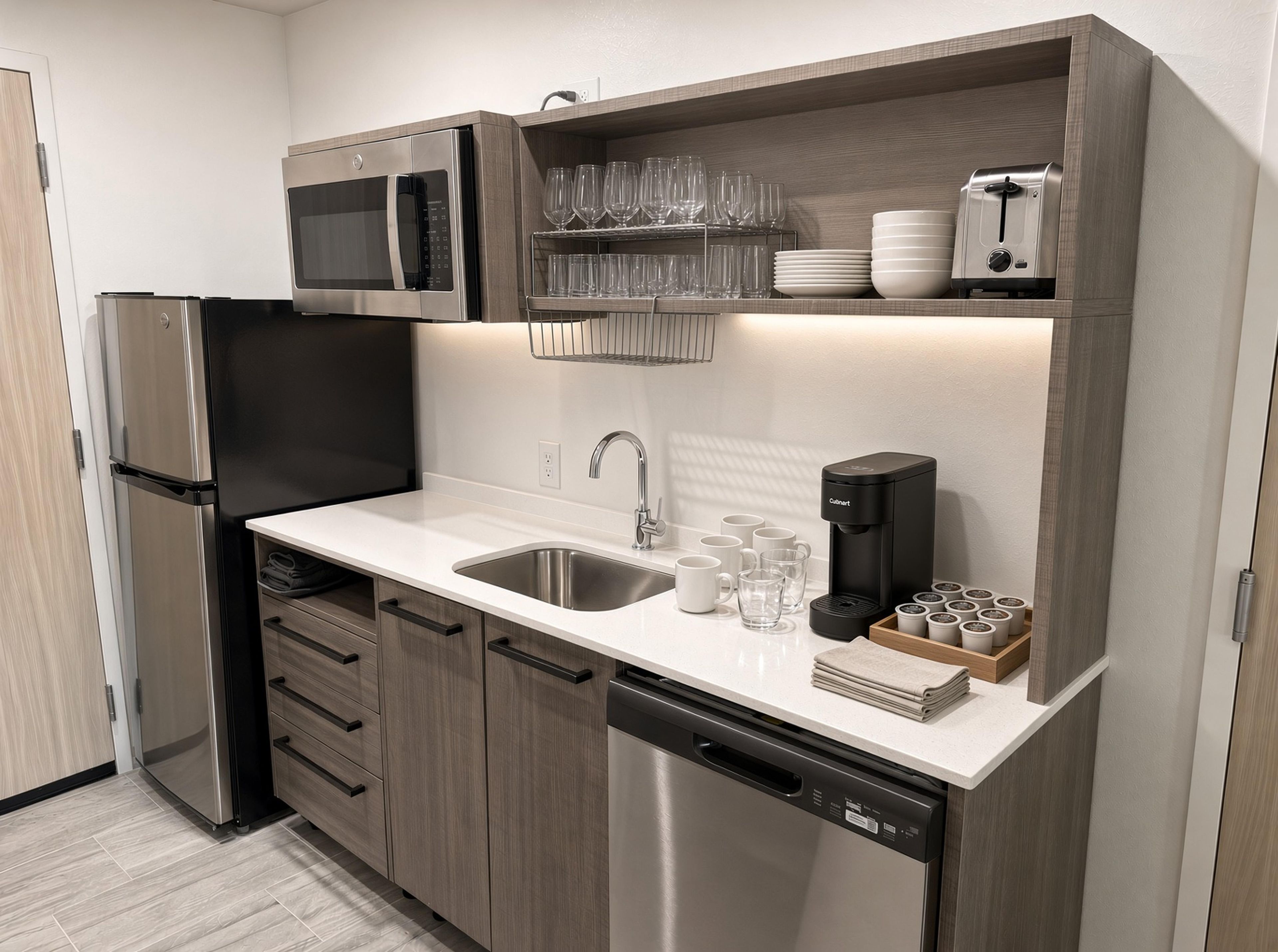 A compact kitchen with a stainless steel refrigerator, a built-in microwave, a coffee maker, and a dishwasher.